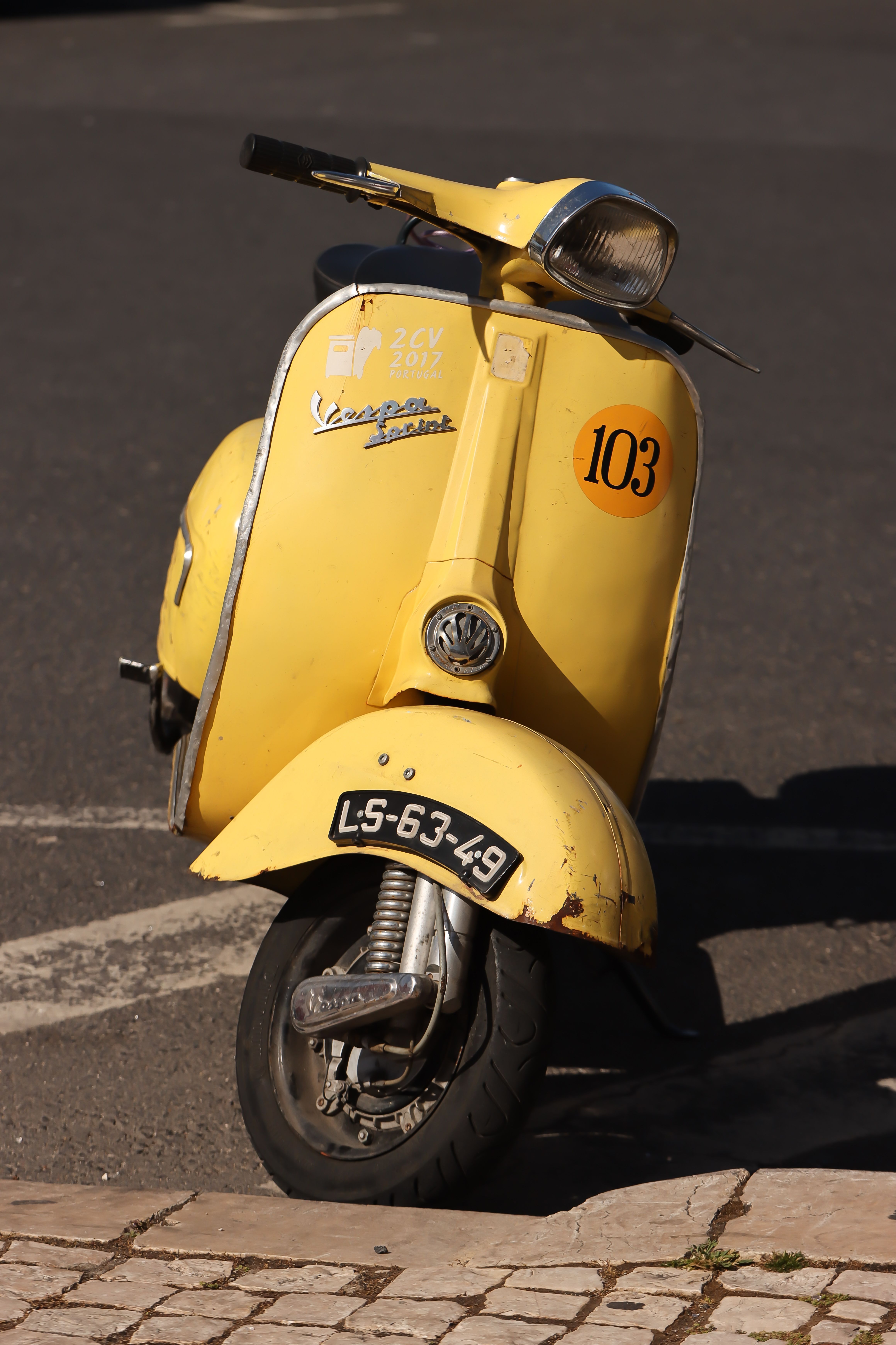 A vintage yellow Vespa scooter parked on a Lisbon street, basking in the sunlight.
