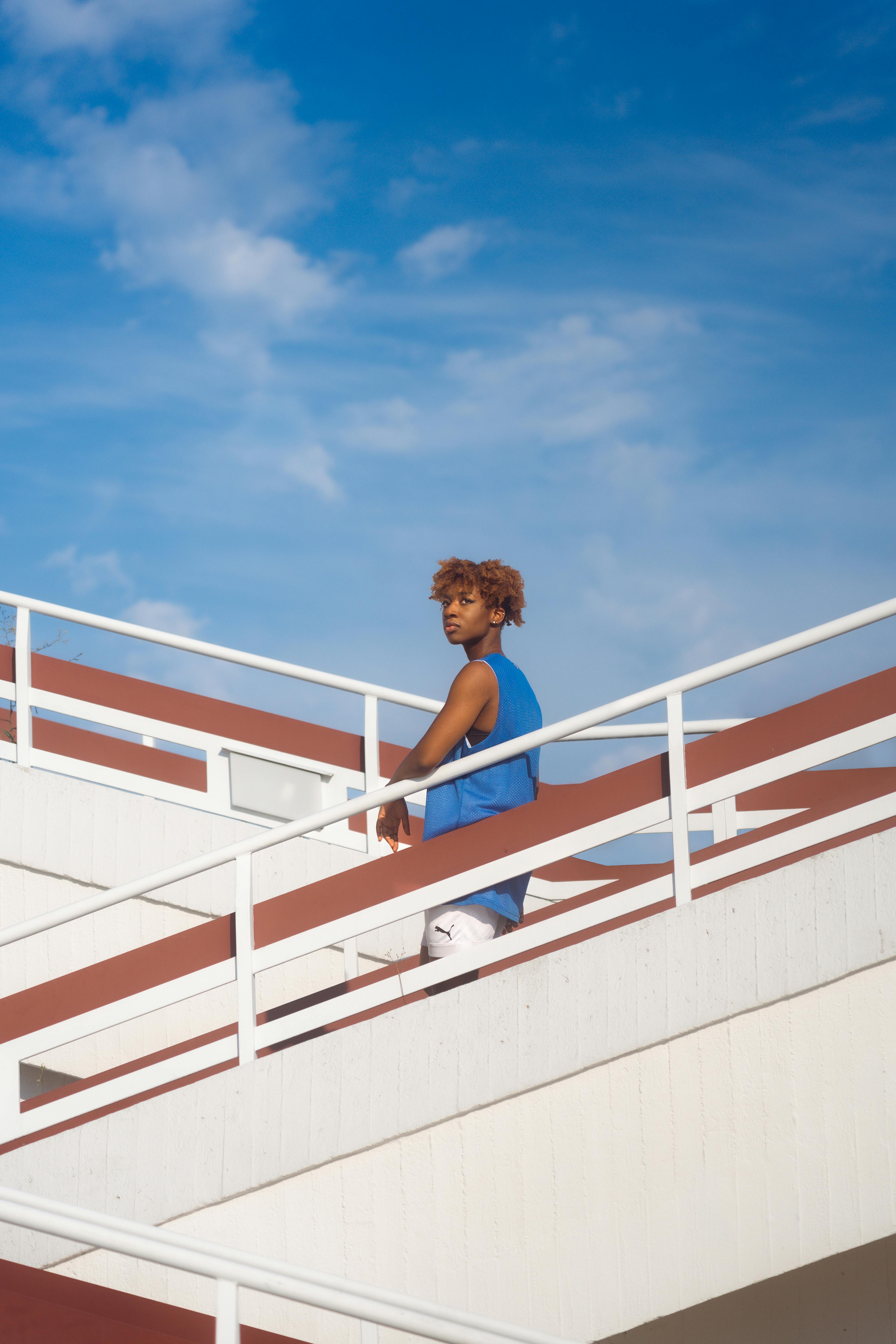 A person poses outdoors on a modern staircase under a clear blue sky.