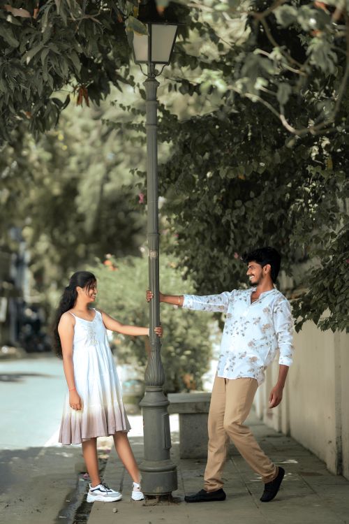 Free A playful couple enjoying a moment around a lamp post on an urban street with greenery. Stock Photo