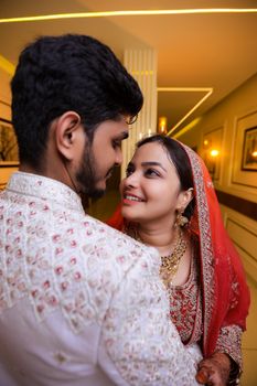 A happy bride and groom embracing in traditional Indian attire indoors.