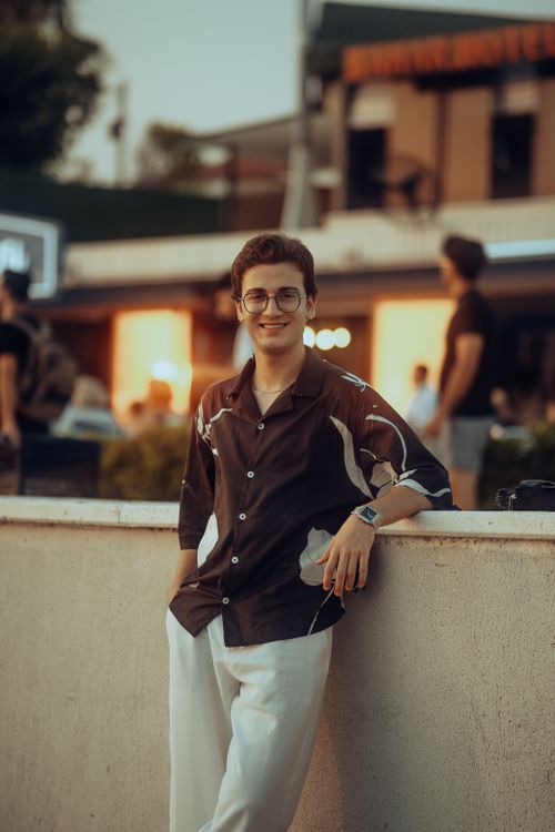 Free Portrait of a young man smiling, wearing eyeglasses, leaning against a wall in an urban setting during the day. Stock Photo