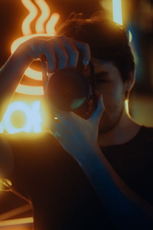 Free A person taking a photo with vibrant neon lights creating a moody atmosphere. Stock Photo