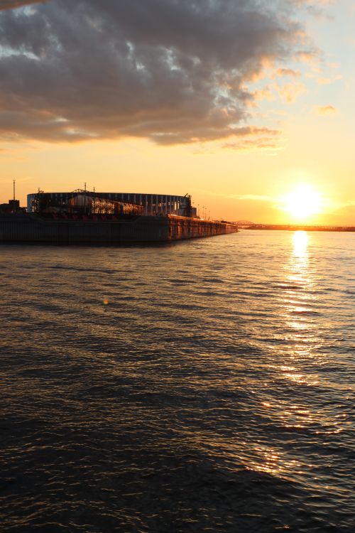 Free Golden sunset over the ocean with an industrial pier silhouetted against the sky. Stock Photo