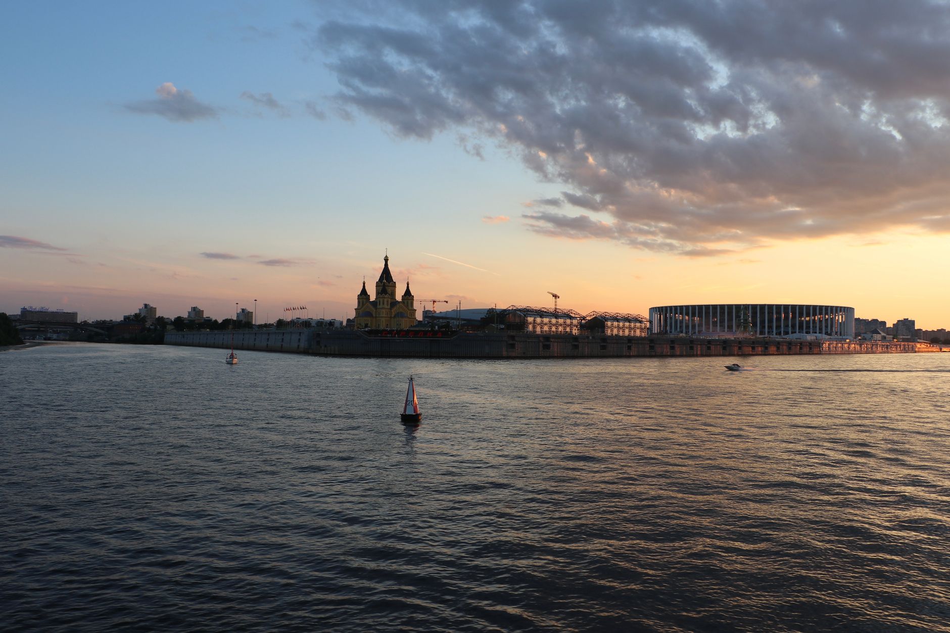 Dusky city skyline with river and boats at sunset, capturing reflection and tranquility.