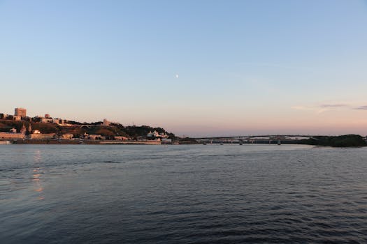 Calm river scene with cityscape and bridge under a fading sunset sky.