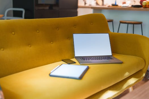 A modern living room featuring a yellow sofa with a laptop, tablet, and smartphone.