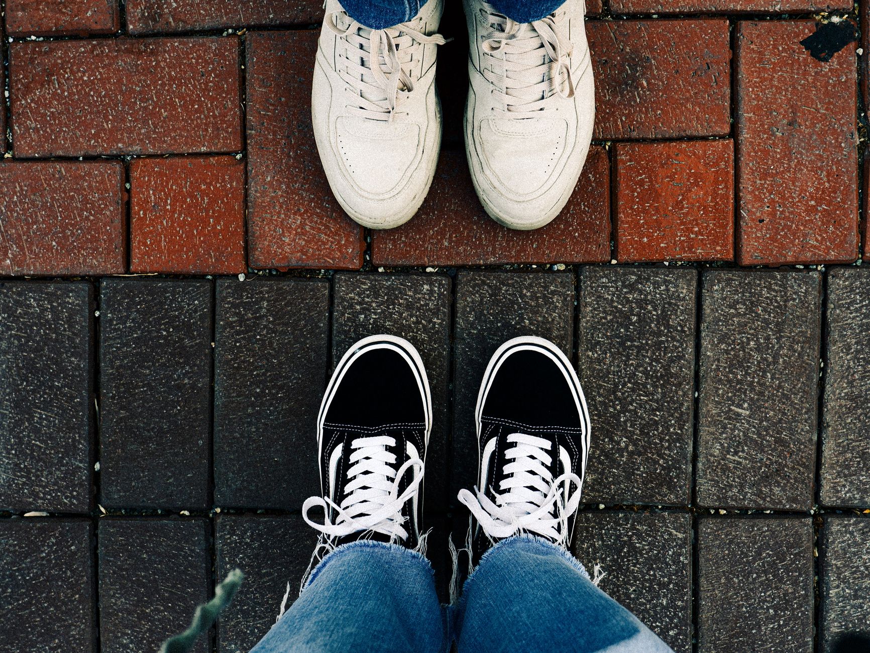 Two pairs of sneakers on a brick pavement, showcasing casual street fashion style.