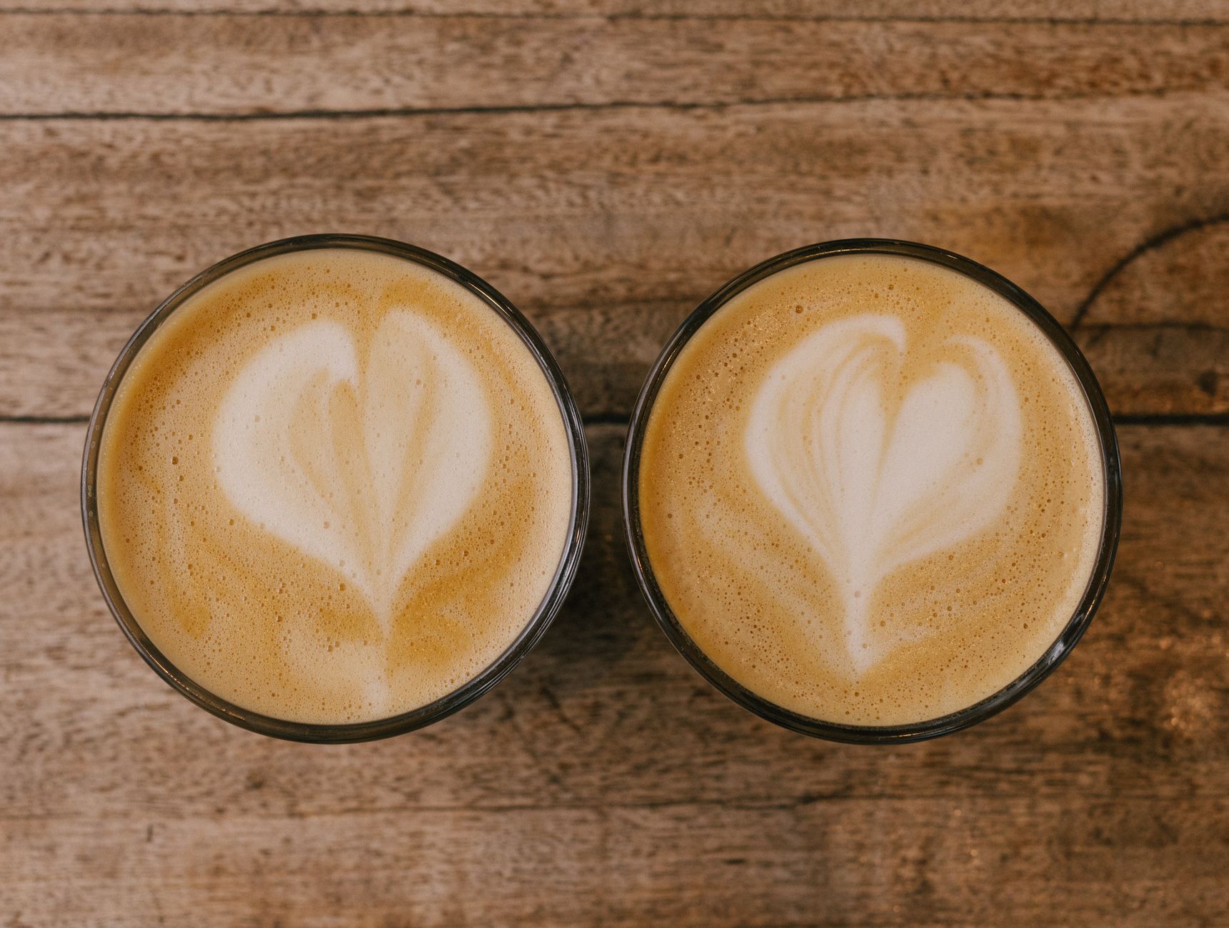 Close-up of two cappuccinos with heart-shaped latte art on a rustic wooden table.