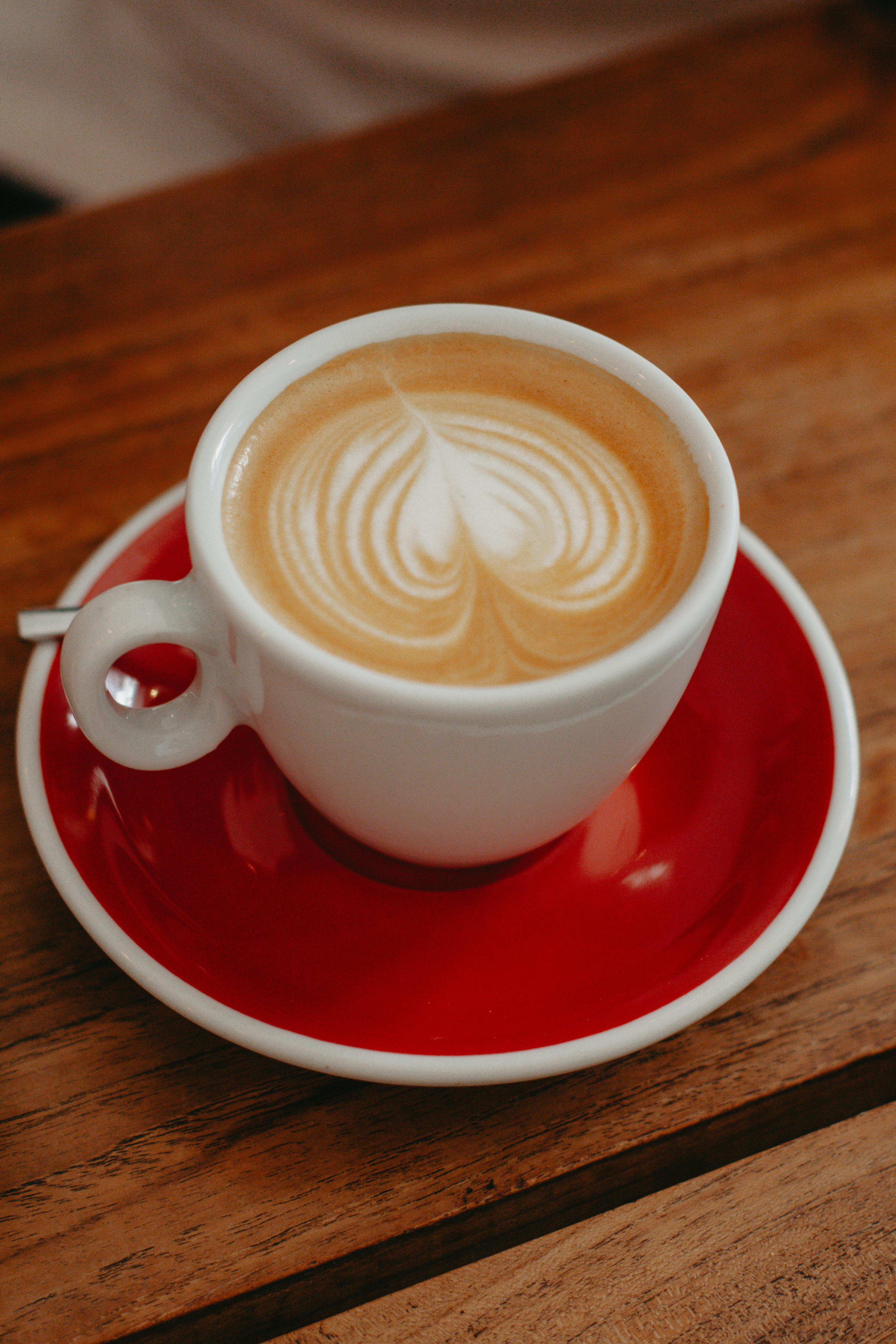 Close-up of a cappuccino with intricate latte art in a red saucer on a wooden table.