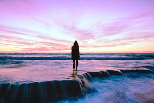 Silhouette Photography of Woman Standing on Seashore during Golden Hour