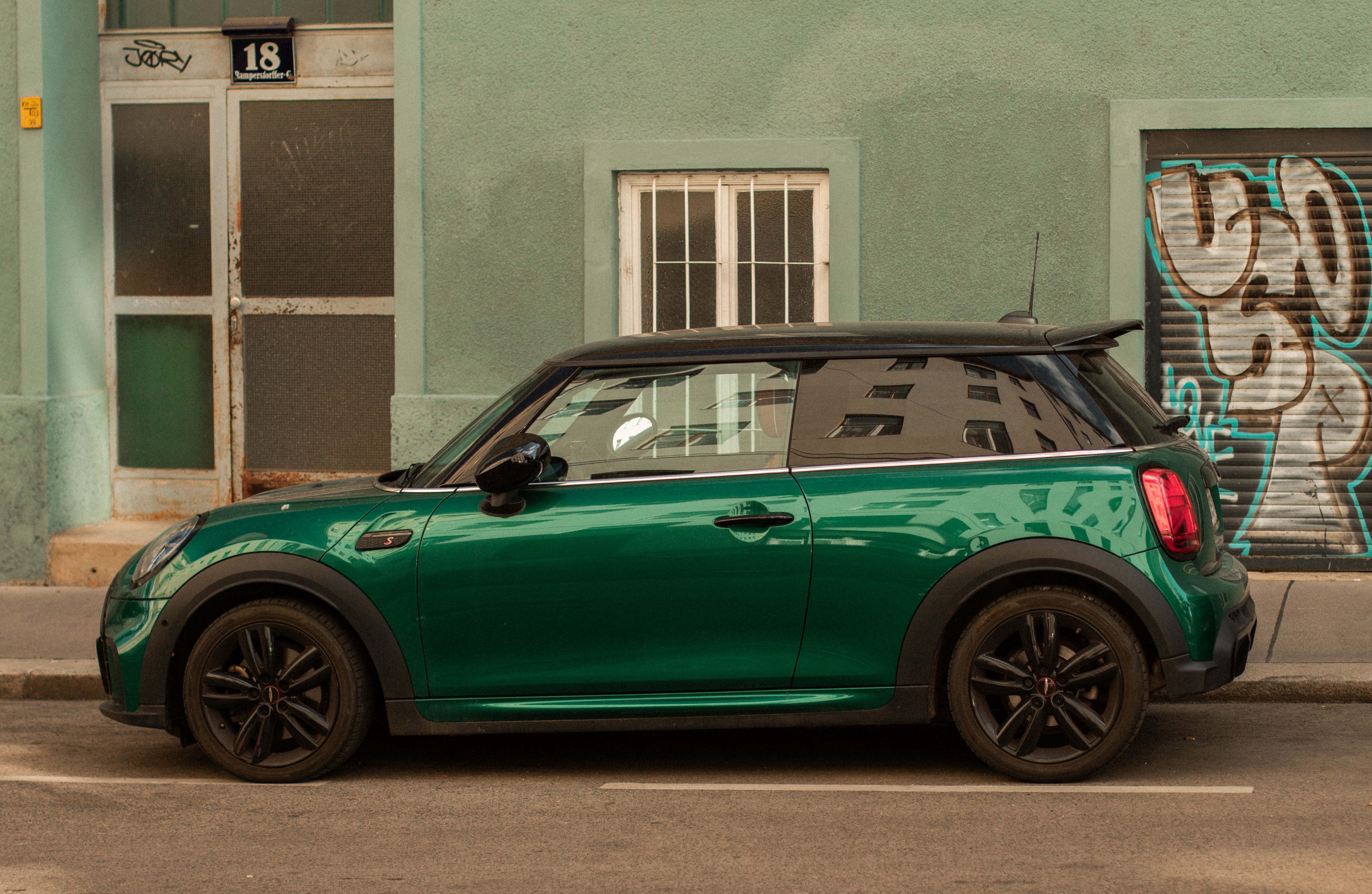 Modern green car parked on an urban street with graffiti walls.