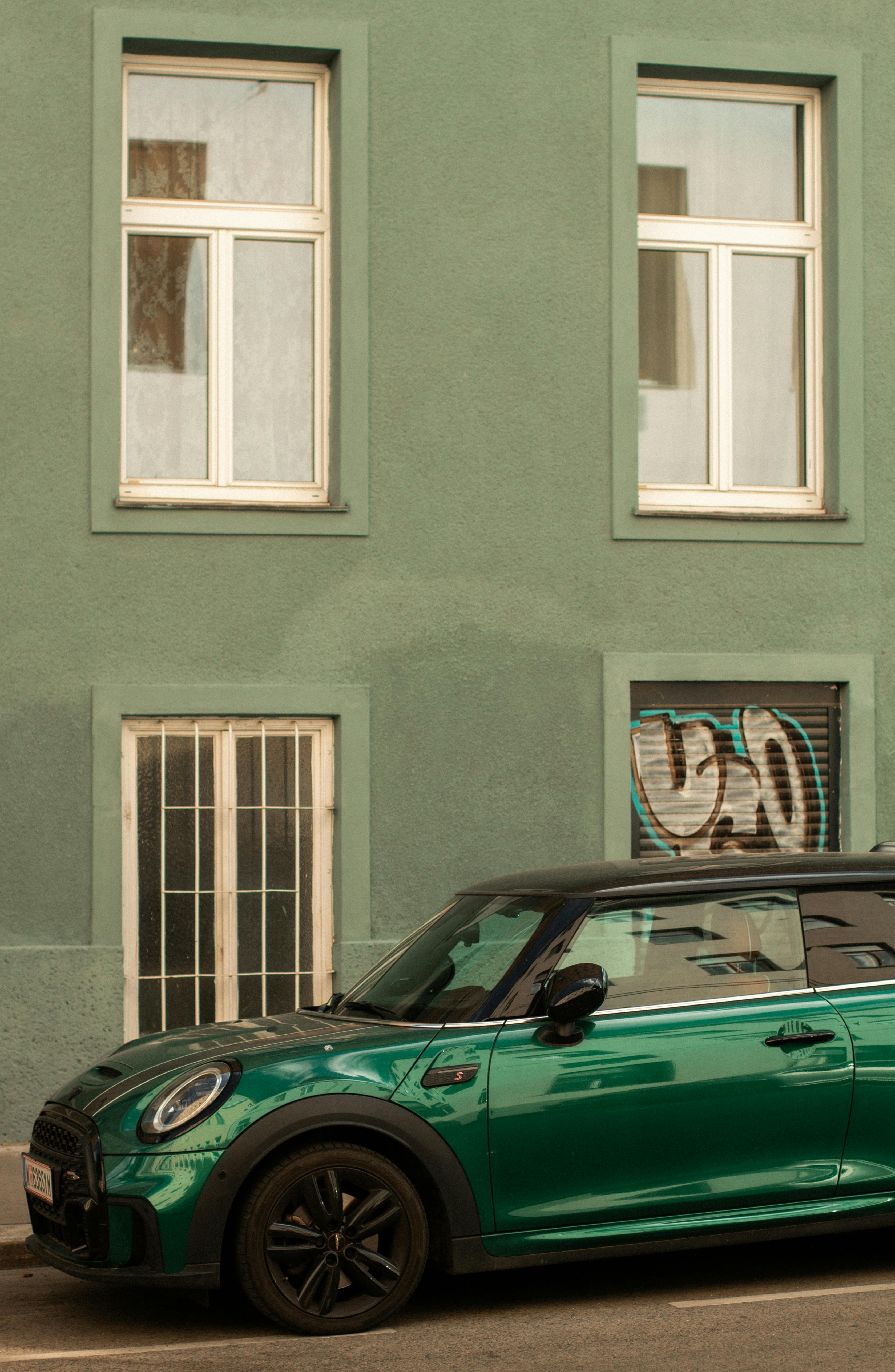 Vintage green car parked on a street against a green building facade.