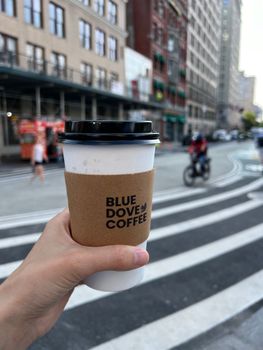 Hand holding cup of Blue Dove Coffee in bustling urban street setting.