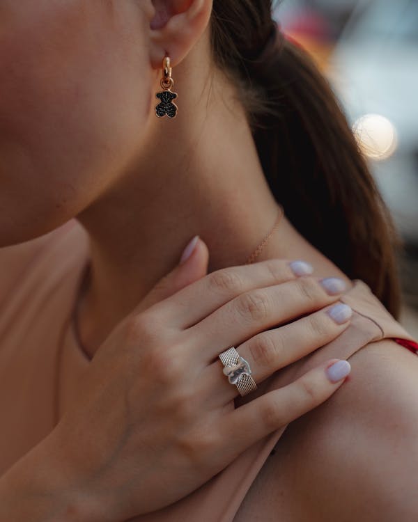 Crop woman with gold earings demonstrating hand with manicure and precious ring on ring finger