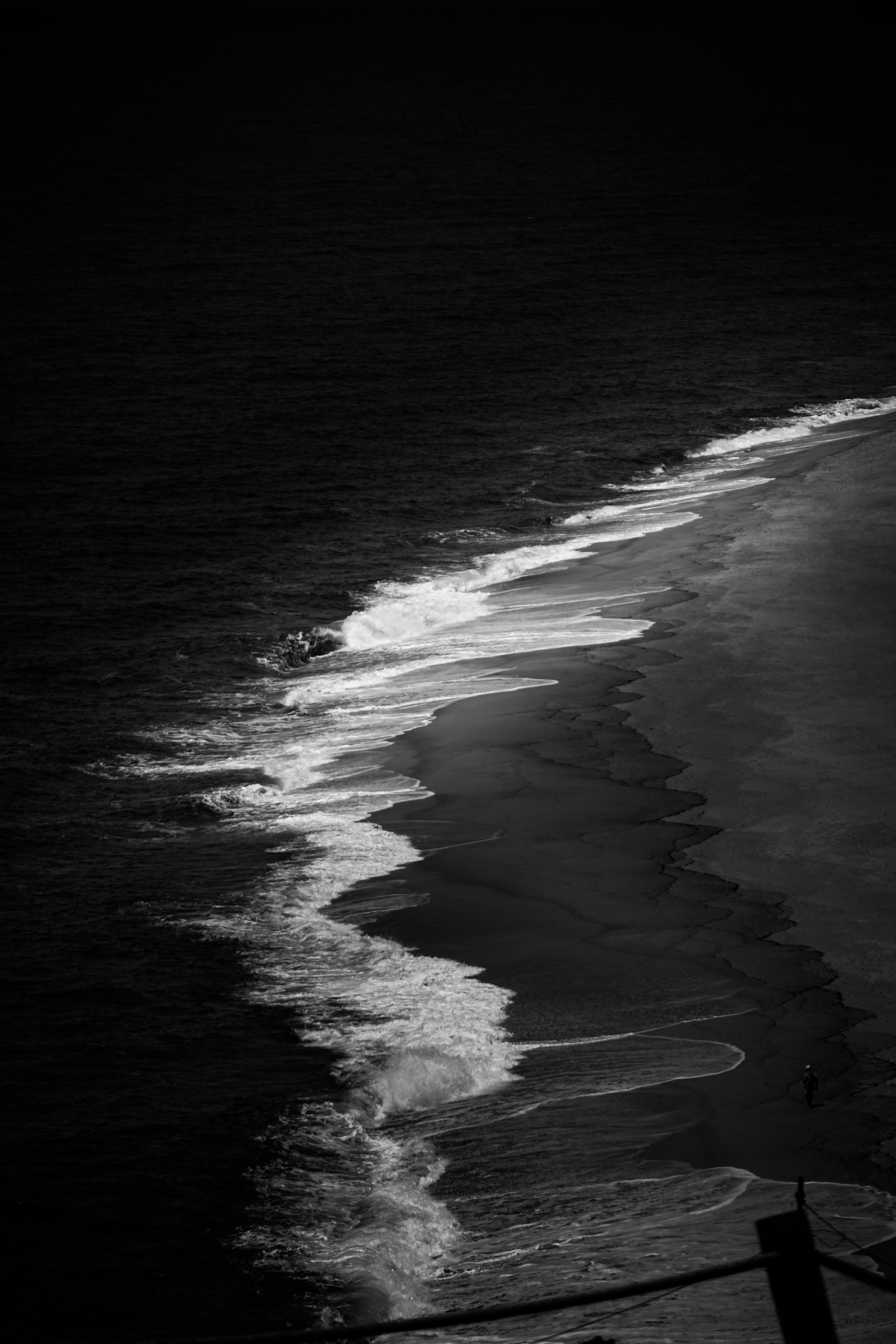 Captivating black and white aerial shot of ocean waves gently crashing onto a secluded beach.