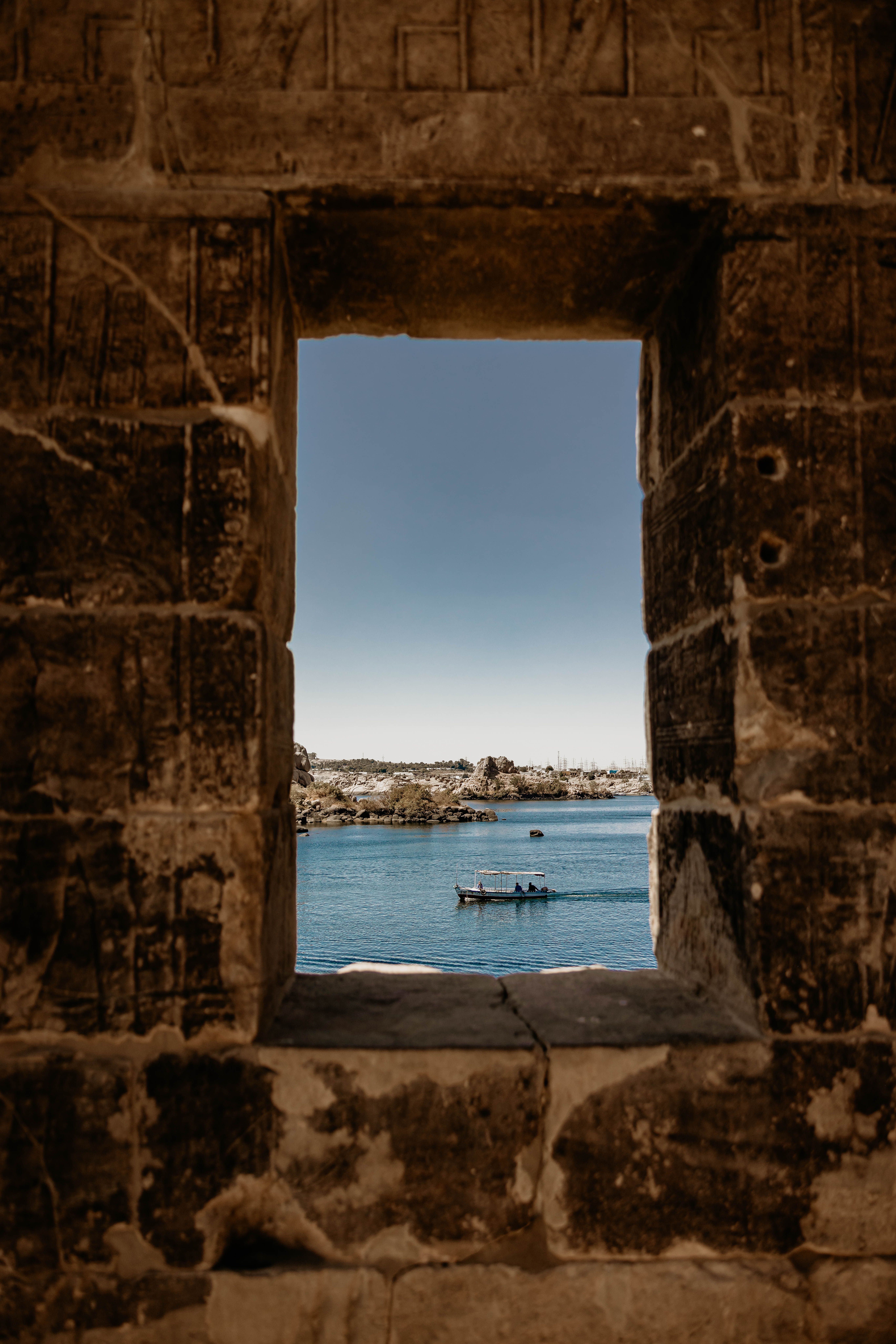 A captivating view of a boat on the Nile through an ancient stone window in Aswan, Egypt.
