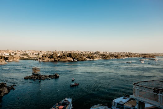 A picturesque view of Aswan's Nile River with boats and lush shoreline under a clear blue sky.