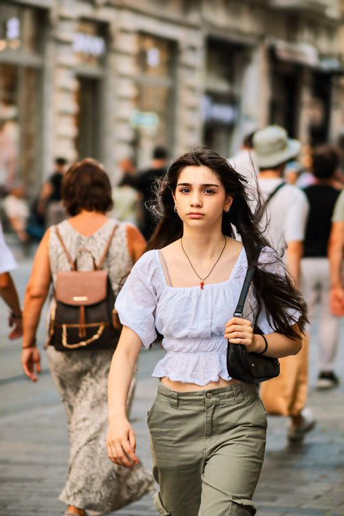 Free A young woman confidently walks through a lively urban street during the day. Stock Photo