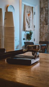 Espresso portafilter on cafe table with stacked cups, evoking cozy coffee shop ambience.