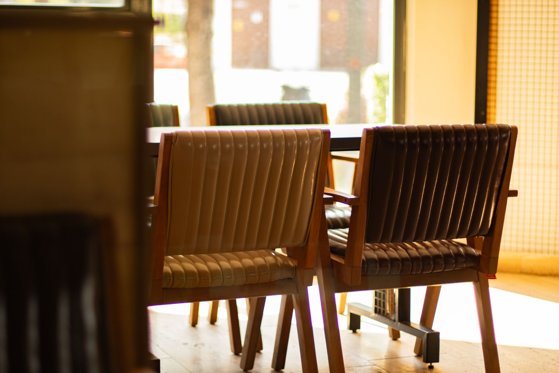A warm, inviting interior with stylish wooden chairs bathed in natural light from large windows.