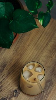 A top view of iced coffee with a straw on a wooden table next to green leaves.