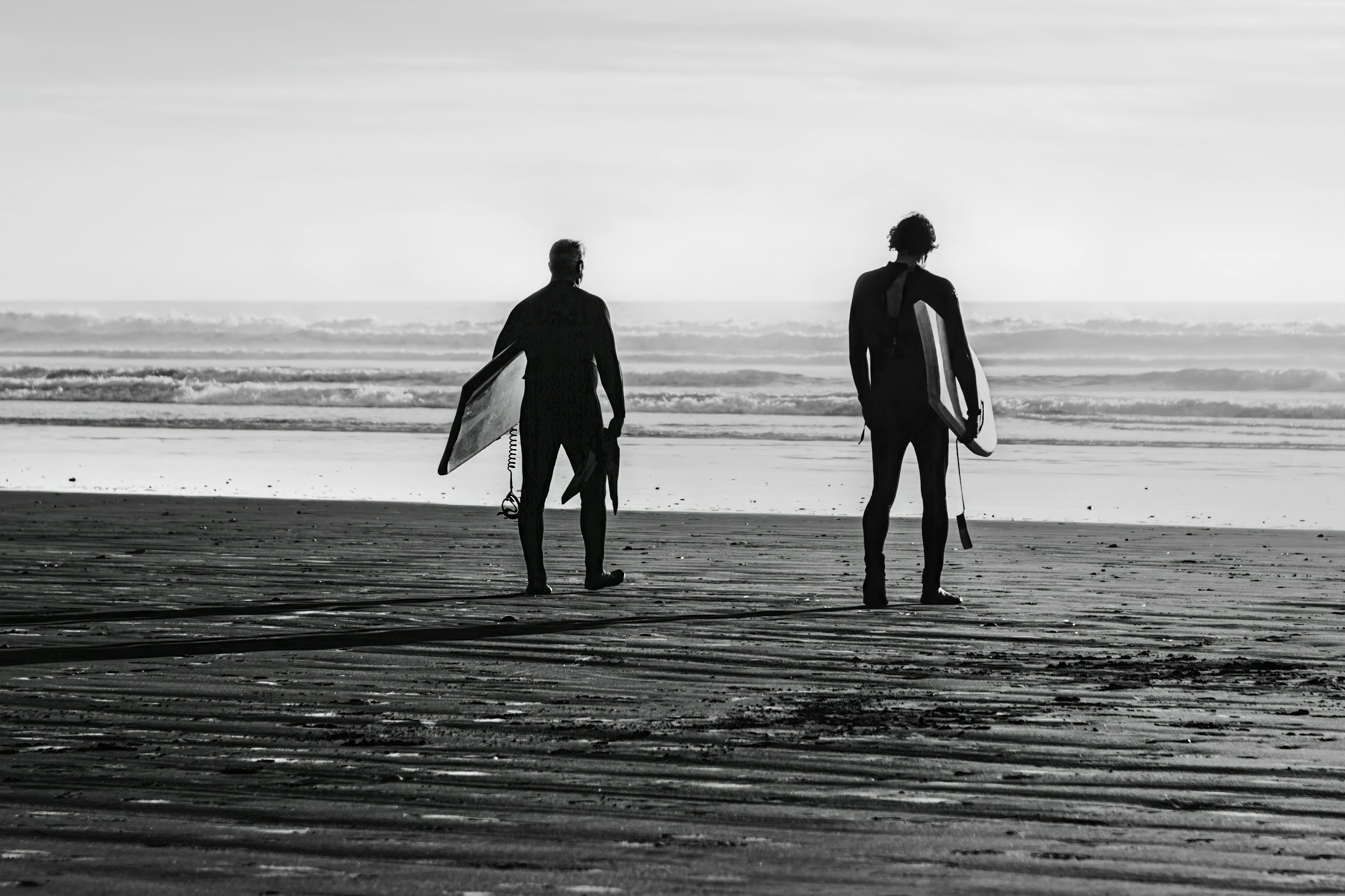 Surfers walk along the sandy shores of Pismo Beach at sunset, holding surfboards and wearing wetsuits.