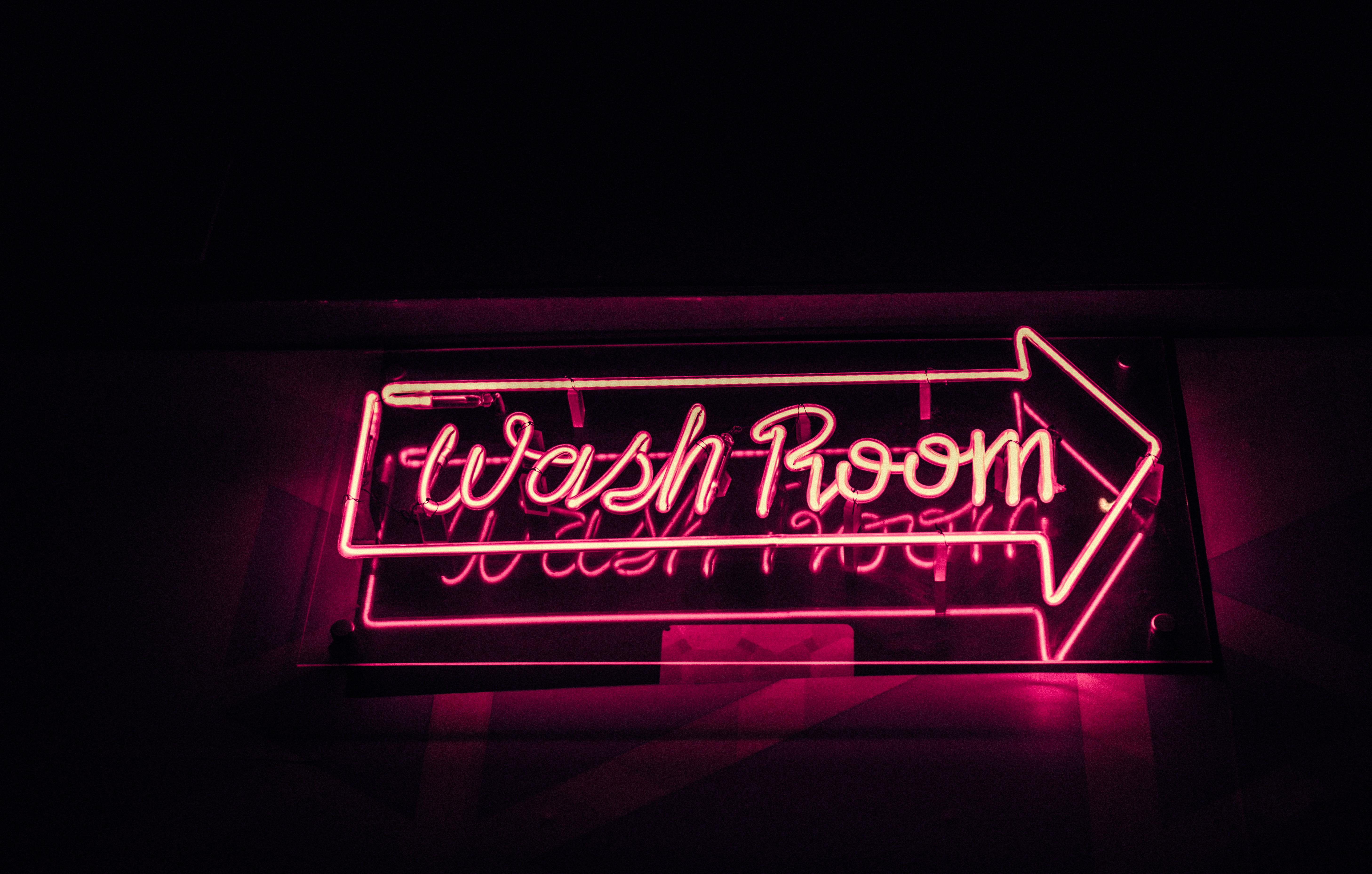 Bright pink neon washroom sign glowing in a dark environment, creating a vibrant and modern ambiance.