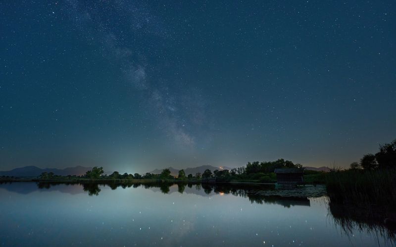 A serene night sky over Chiemsee, Germany, featuring stars and lake reflections.