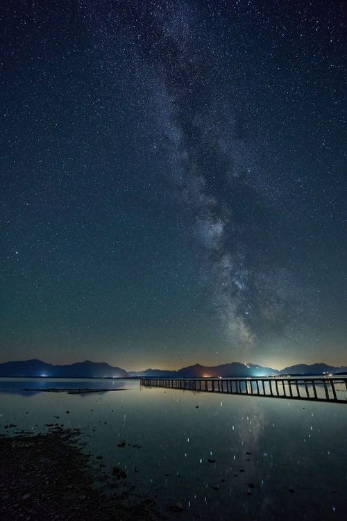 Free A mesmerizing view of the Milky Way over Chiemsee Lake, Germany, reflecting in calm waters. Stock Photo