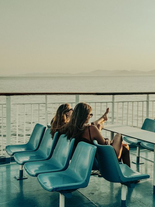 Free Two women enjoying a leisurely moment on a ferry, overlooking the ocean during sunset. Stock Photo