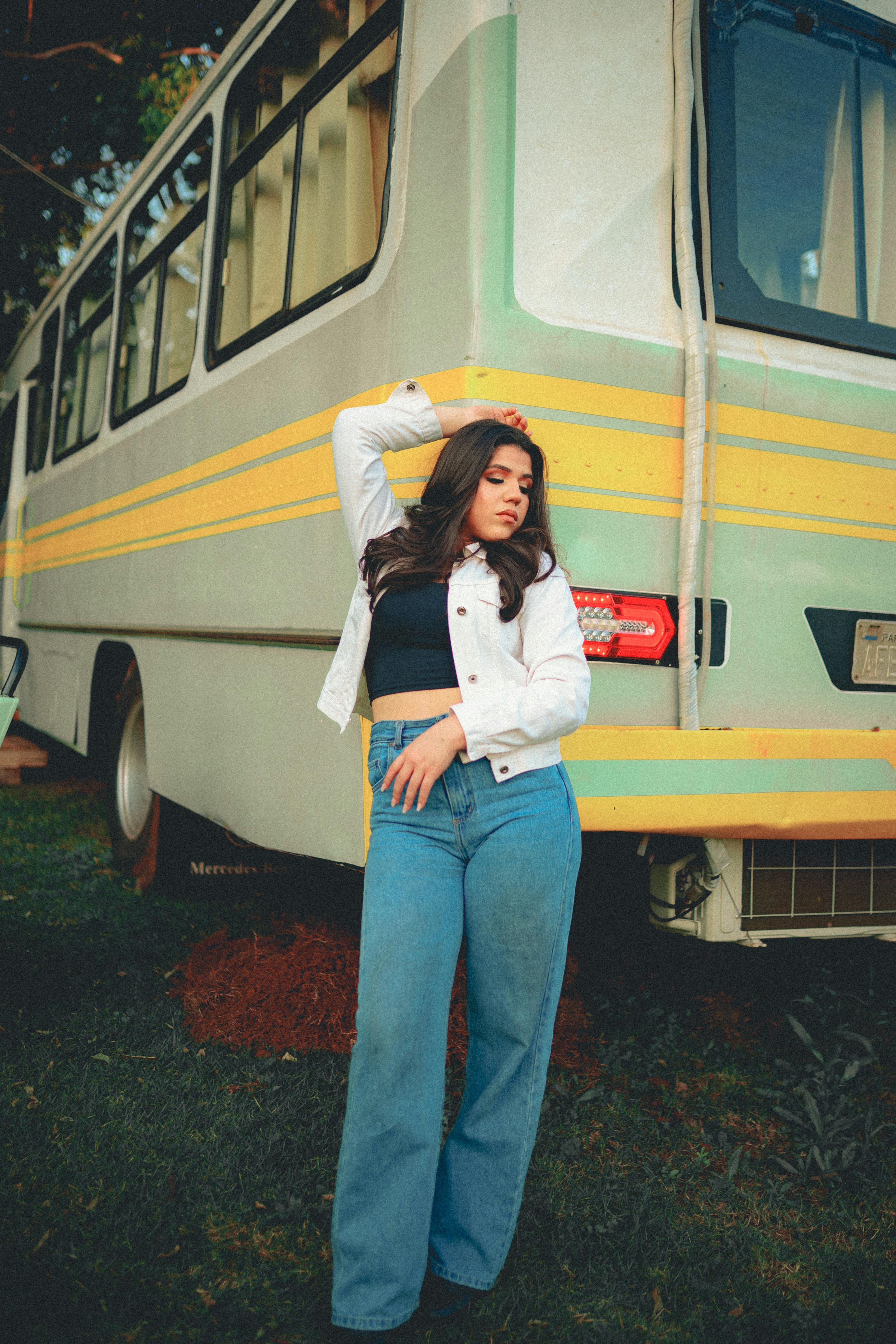 a woman in jeans and a jacket standing next to a bus