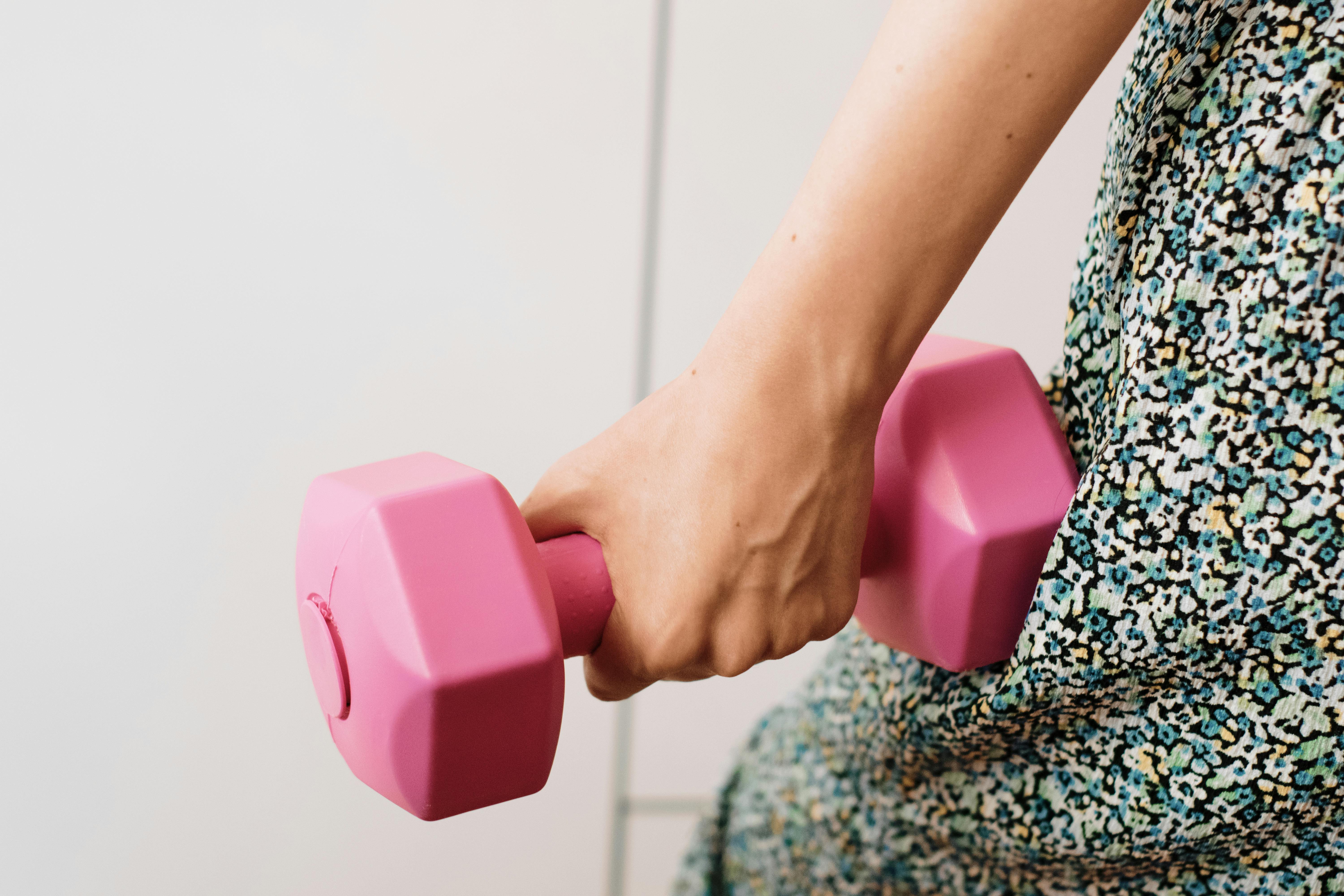 Close-up of a woman's hand holding a pink dumbbell, symbolizing fitness and strength.