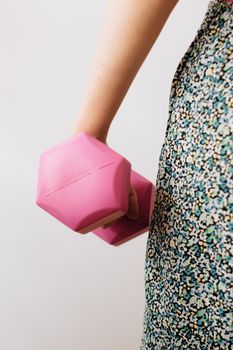 Side profile of a woman holding a pink dumbbell while wearing a floral dress indoors.