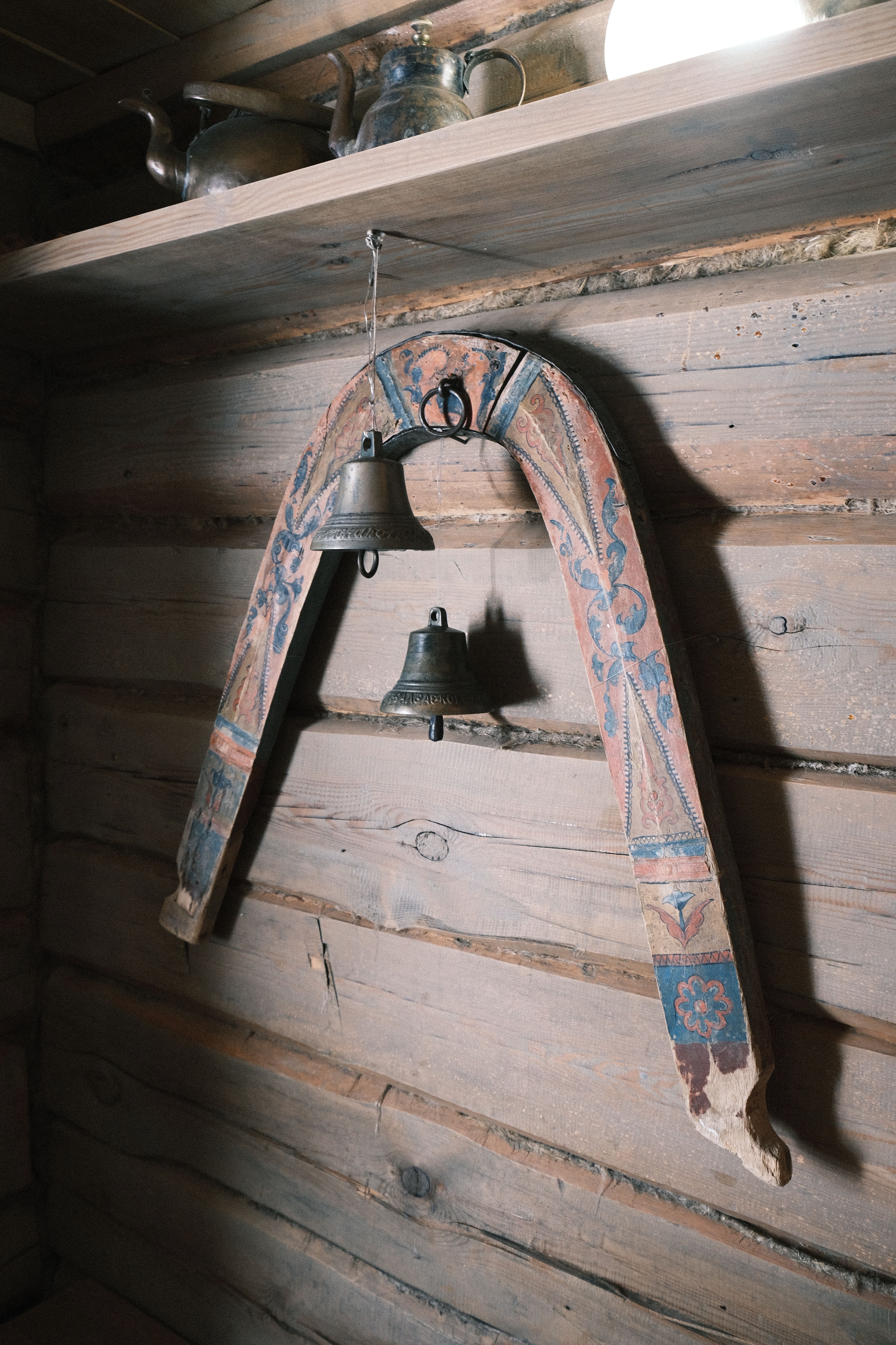 Vintage decorated bells hanging on a rustic wooden wall indoors, creating a historical ambiance.