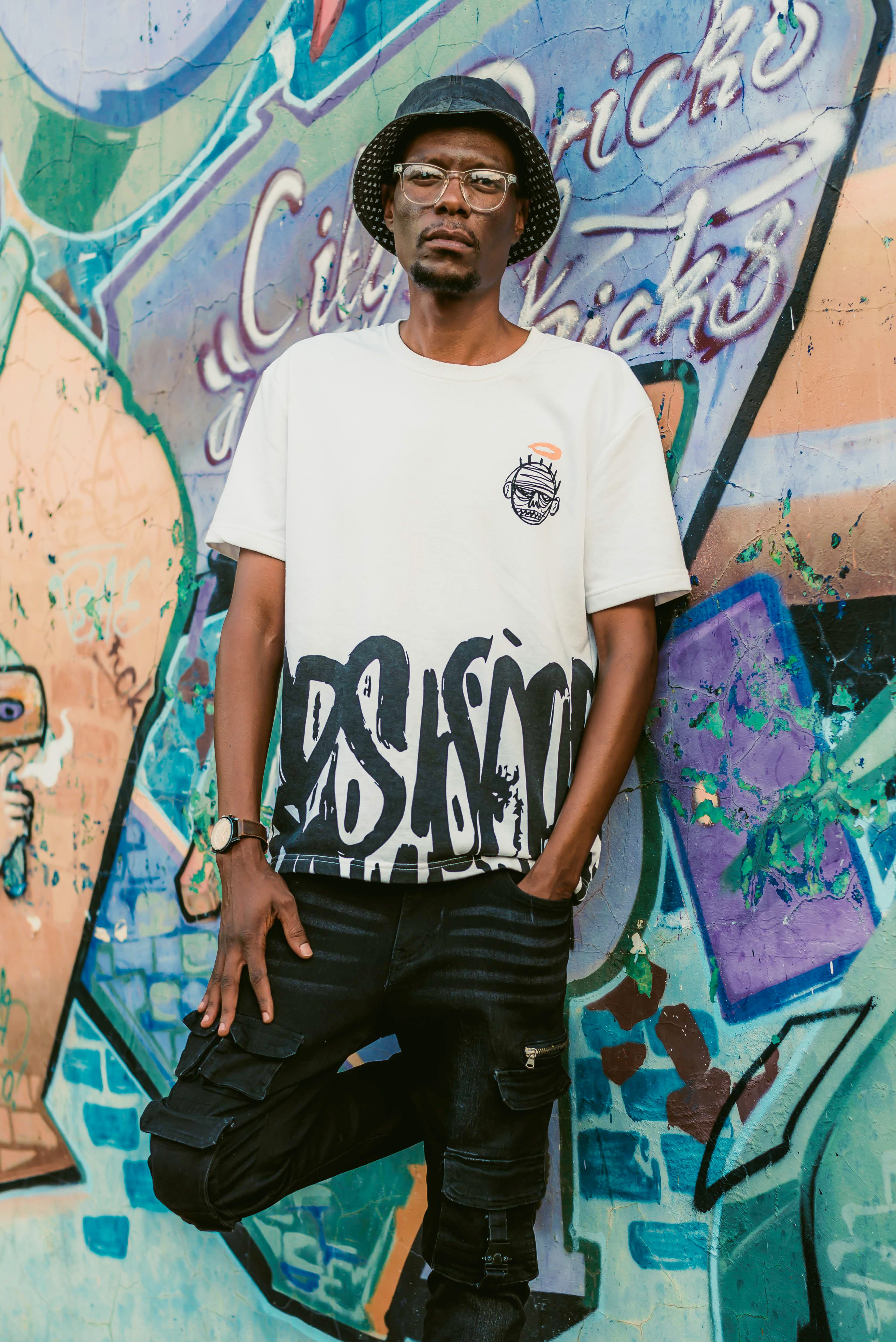 A stylish adult male stands in front of a vibrant graffiti wall.