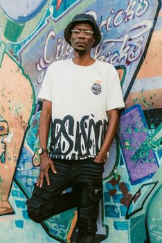 A stylish adult male stands in front of a vibrant graffiti wall.