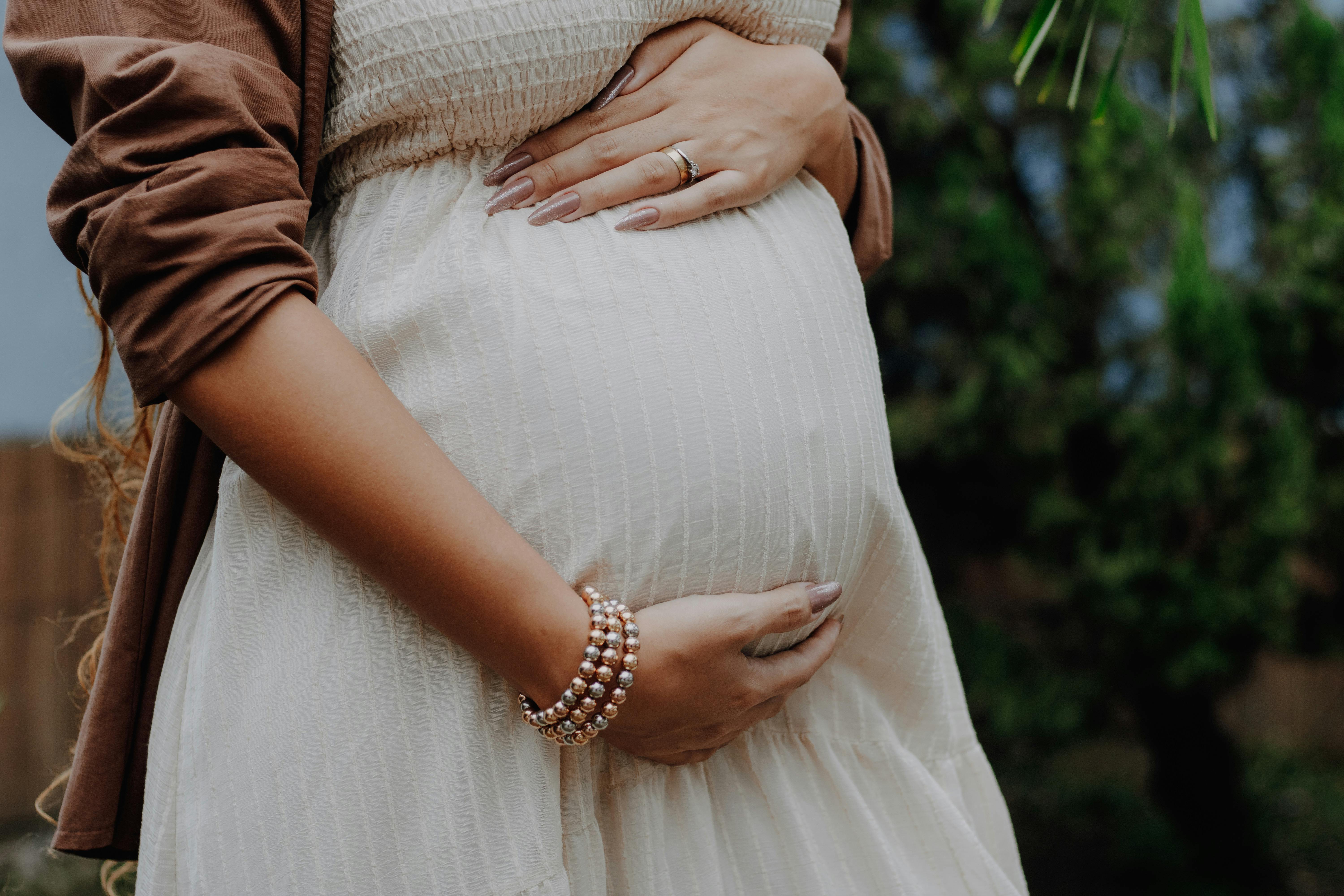 A calm outdoor portrait of a pregnant woman gently cradling her belly, symbolizing love and anticipation.
