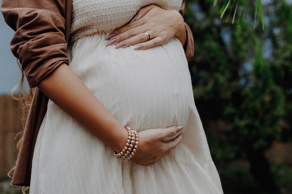 A calm outdoor portrait of a pregnant woman gently cradling her belly, symbolizing love and anticipation.