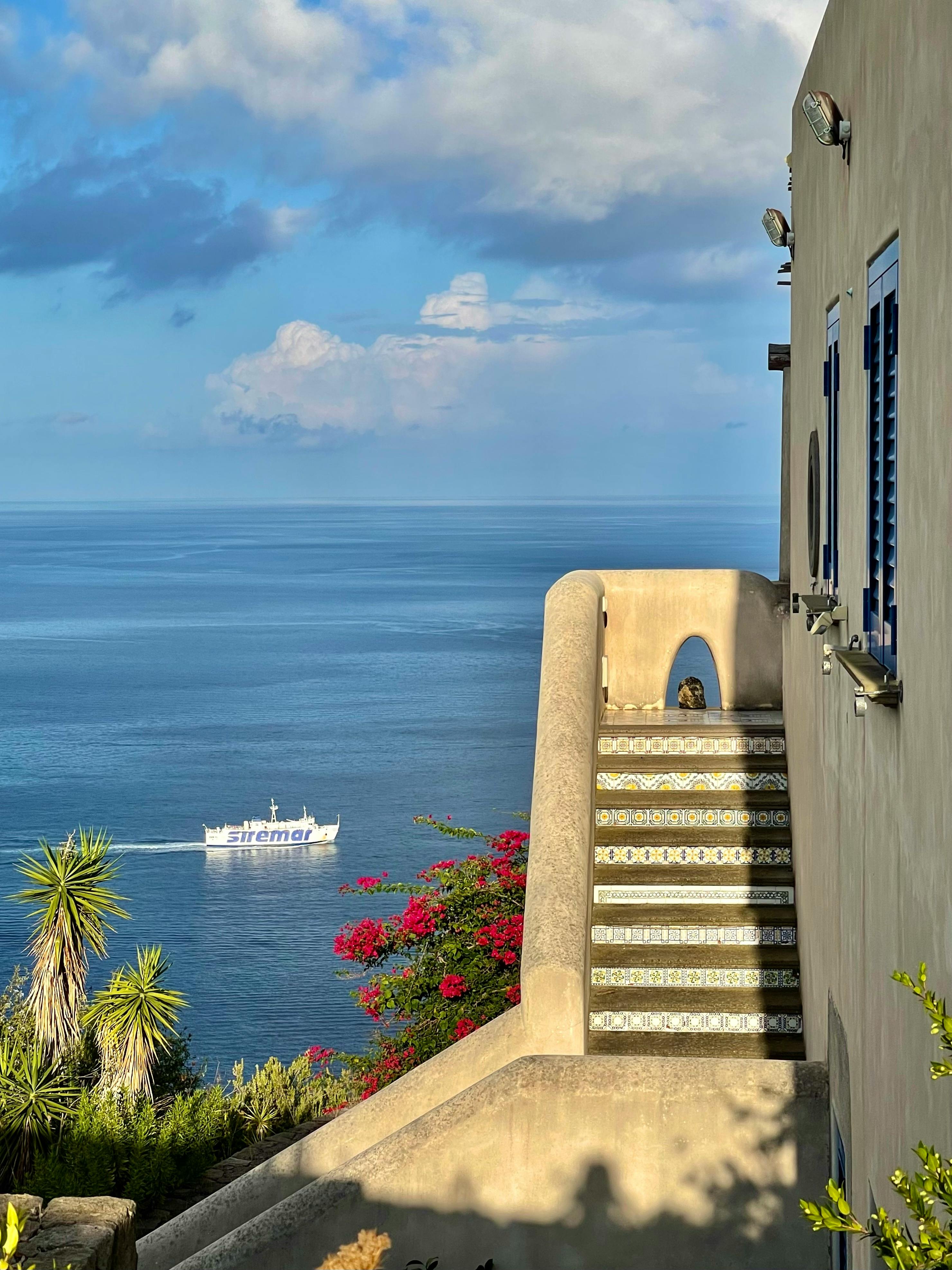 Scenic summer view of the sea and stairs in Sicilì, Italy with a boat and bright blooms.