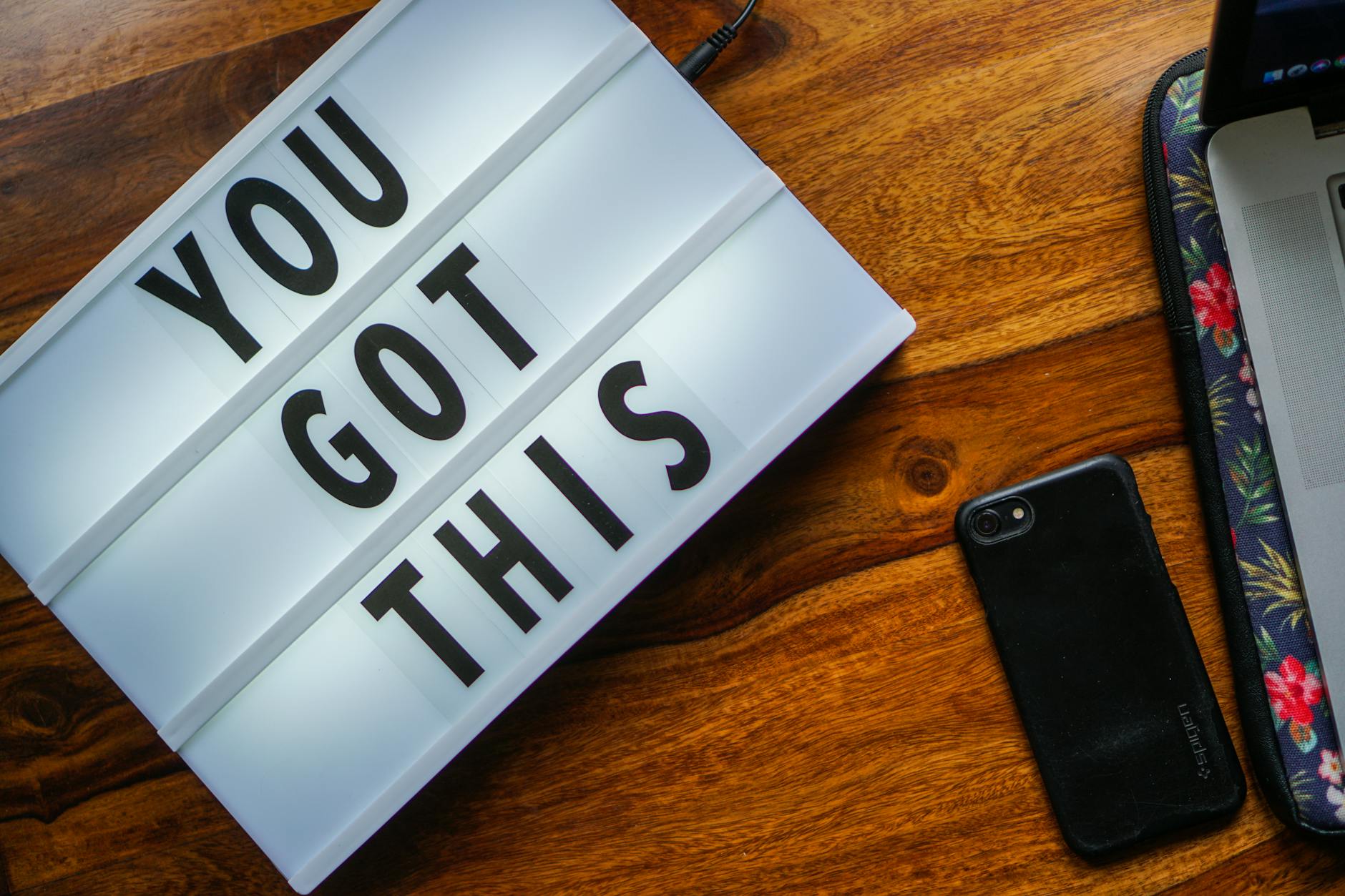 Motivational quote 'You Got This' on a lightbox, smartphone on a wooden table, cozy workspace vibe.