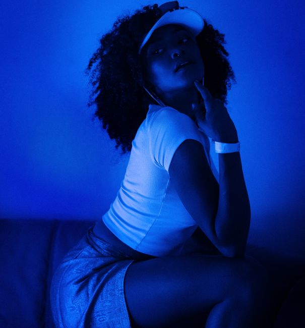 A fashionable woman posing in dramatic blue lighting, showcasing modern style and confidence.
