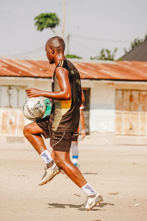 Free A young man skillfully playing soccer on a sandy outdoor field under clear skies. Stock Photo