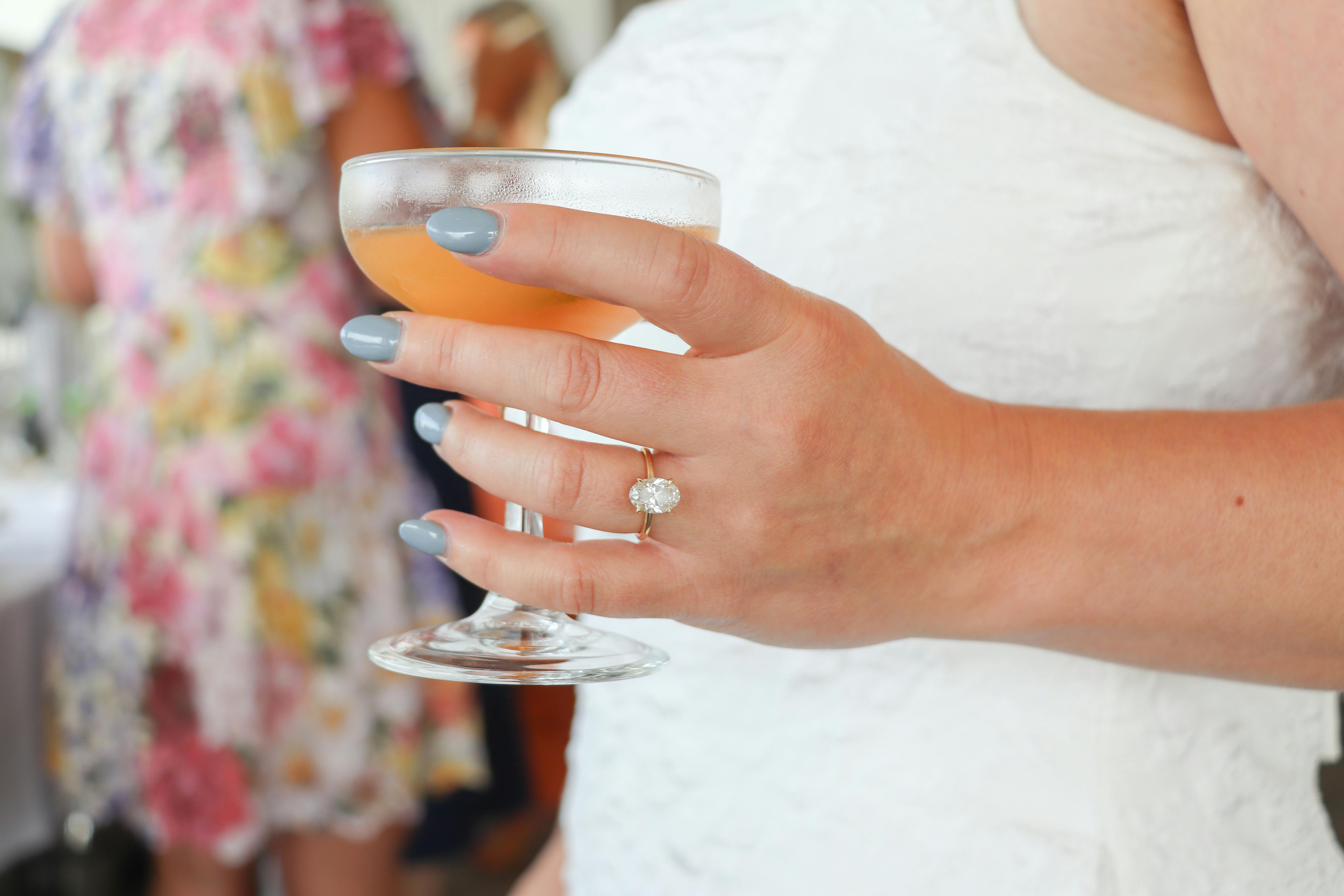 Close-up of a bride's hand with engagement ring holding a cocktail.