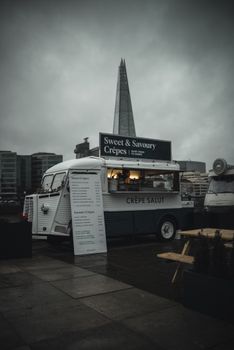 A cozy crepe food truck with The Shard skyscraper in the background, London vibes