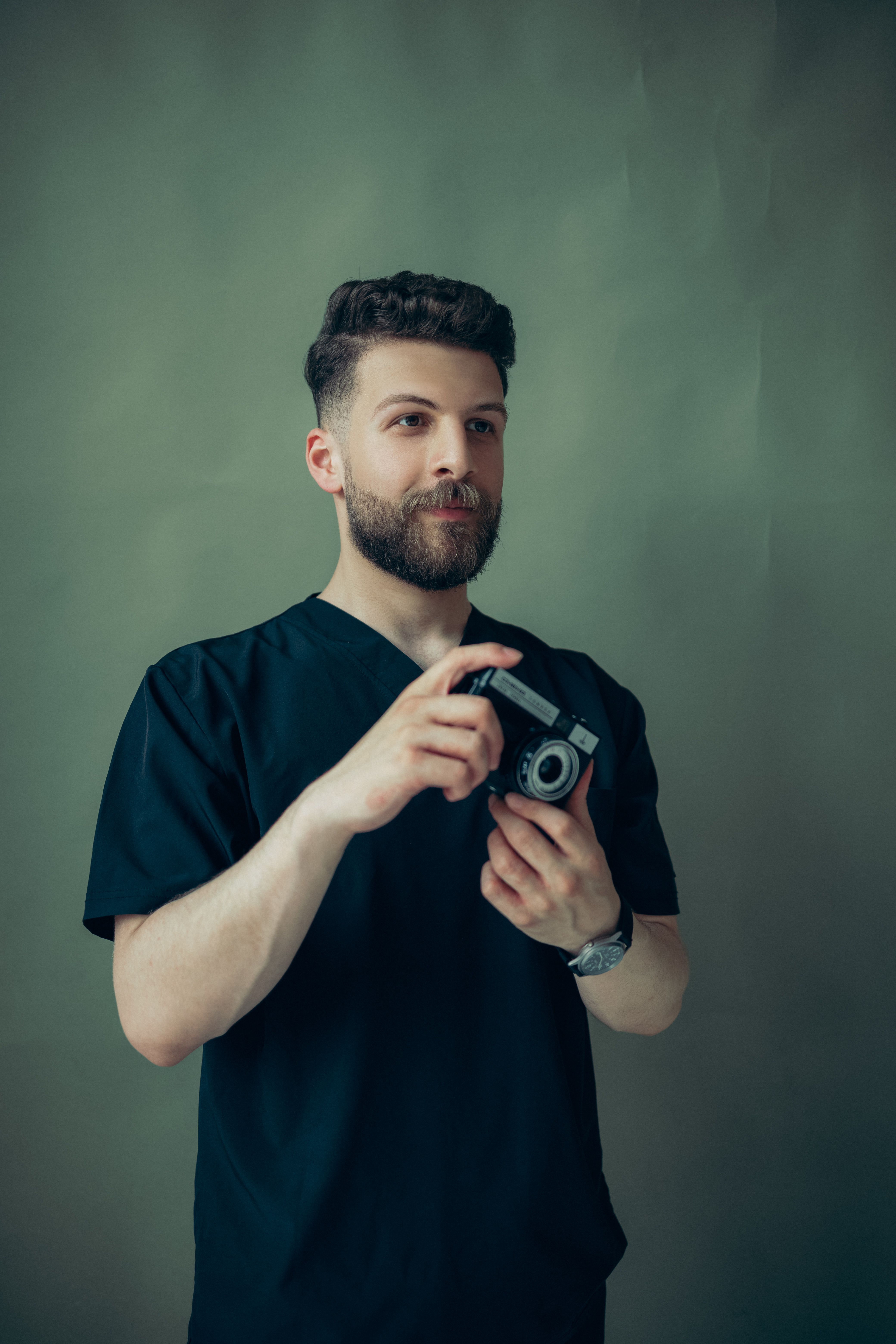 Portrait of a young man holding a vintage camera in a studio setting, exuding a retro style.