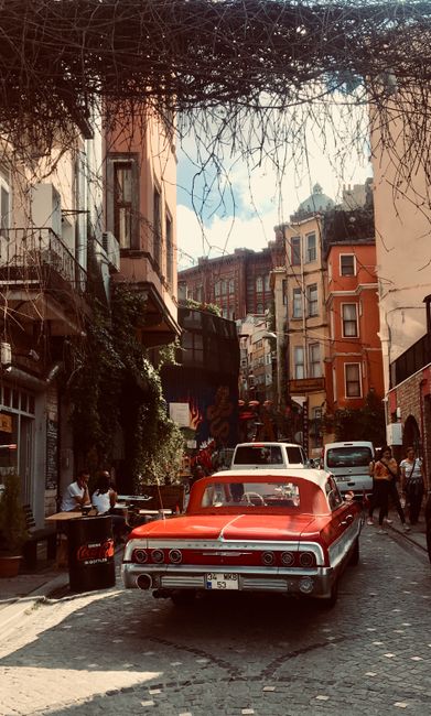 A vibrant urban street with classic car, colorful buildings, and lively atmosphere.