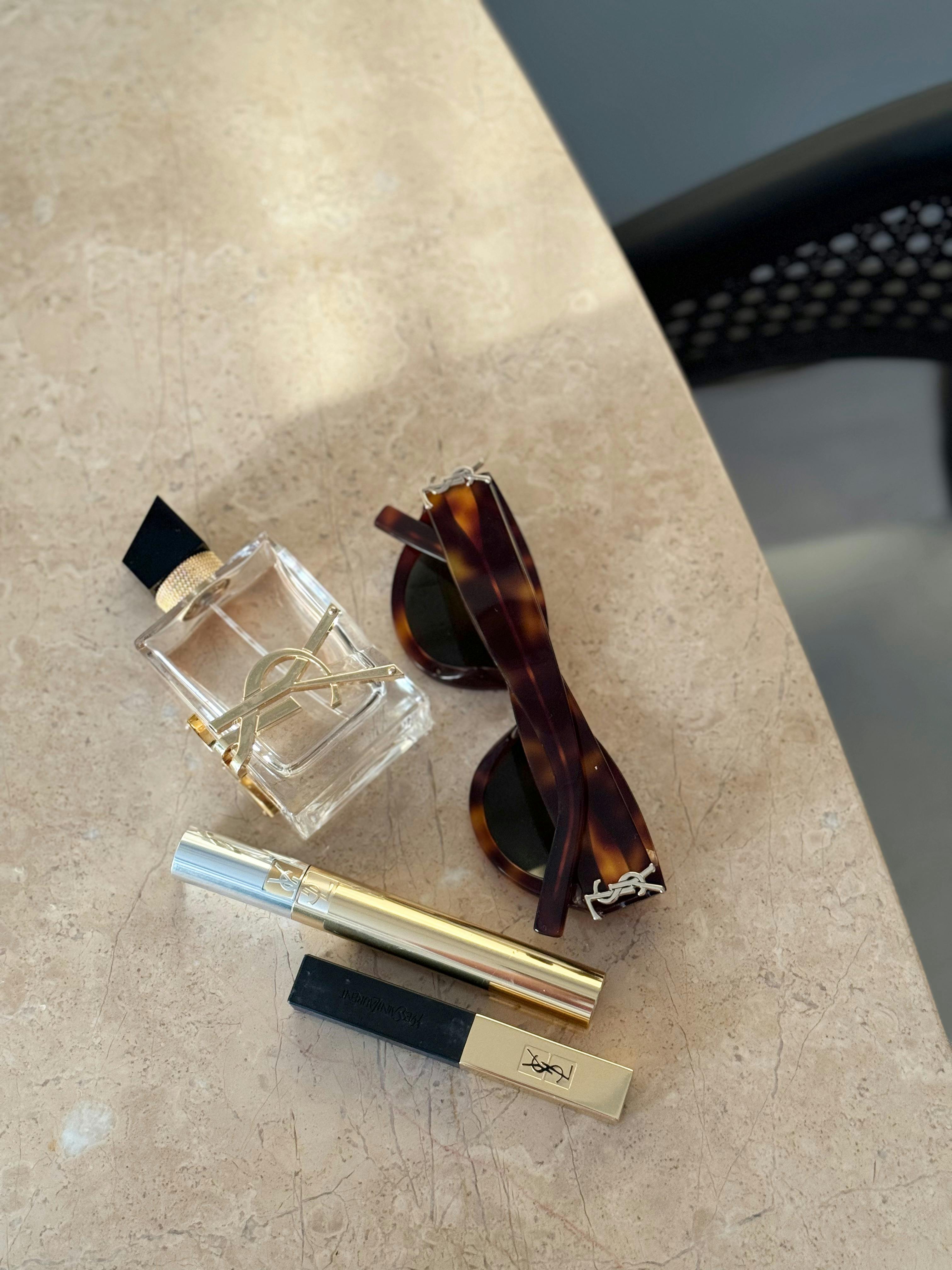 Stylish flat lay featuring sunglasses, perfume, and mascara on a marble surface.