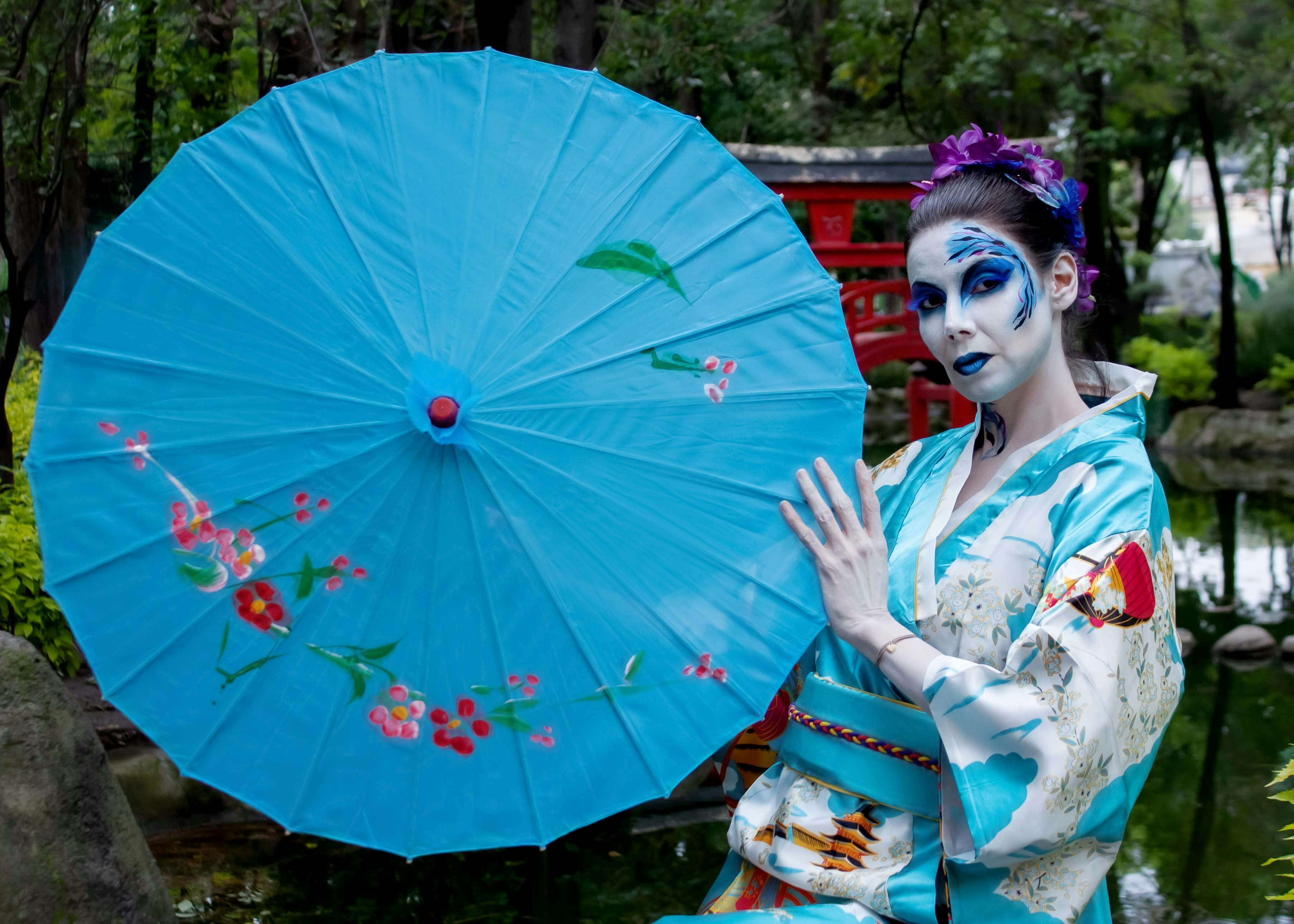 a woman dressed in geisha makeup holding an umbrella