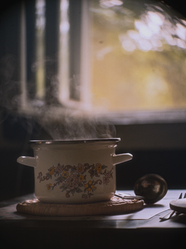 A vintage floral pot emitting steam, set in a warm, cozy kitchen atmosphere.