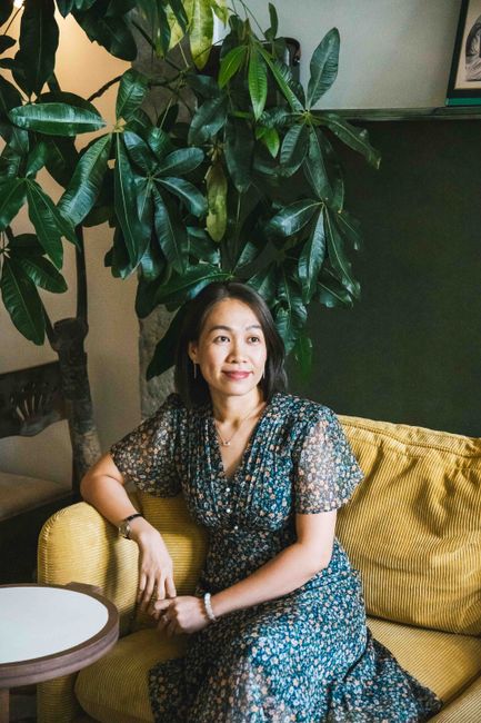 Asian woman sitting in a cozy Ho Chi Minh City cafe, surrounded by plants, exuding elegance and relaxation.
